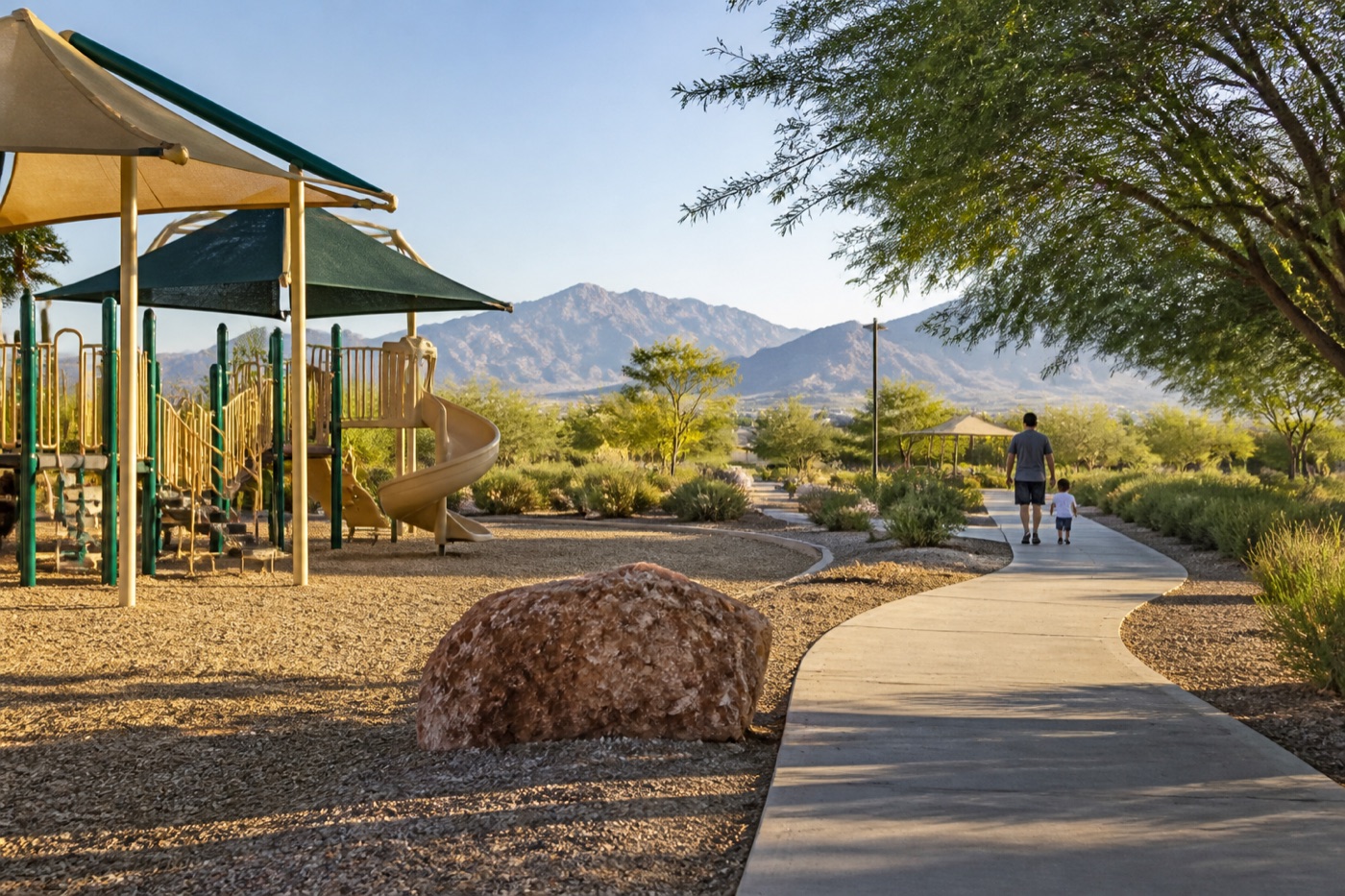 Parent and child walking near a shaded North Las Vegas park playground with desert mountains in the distance